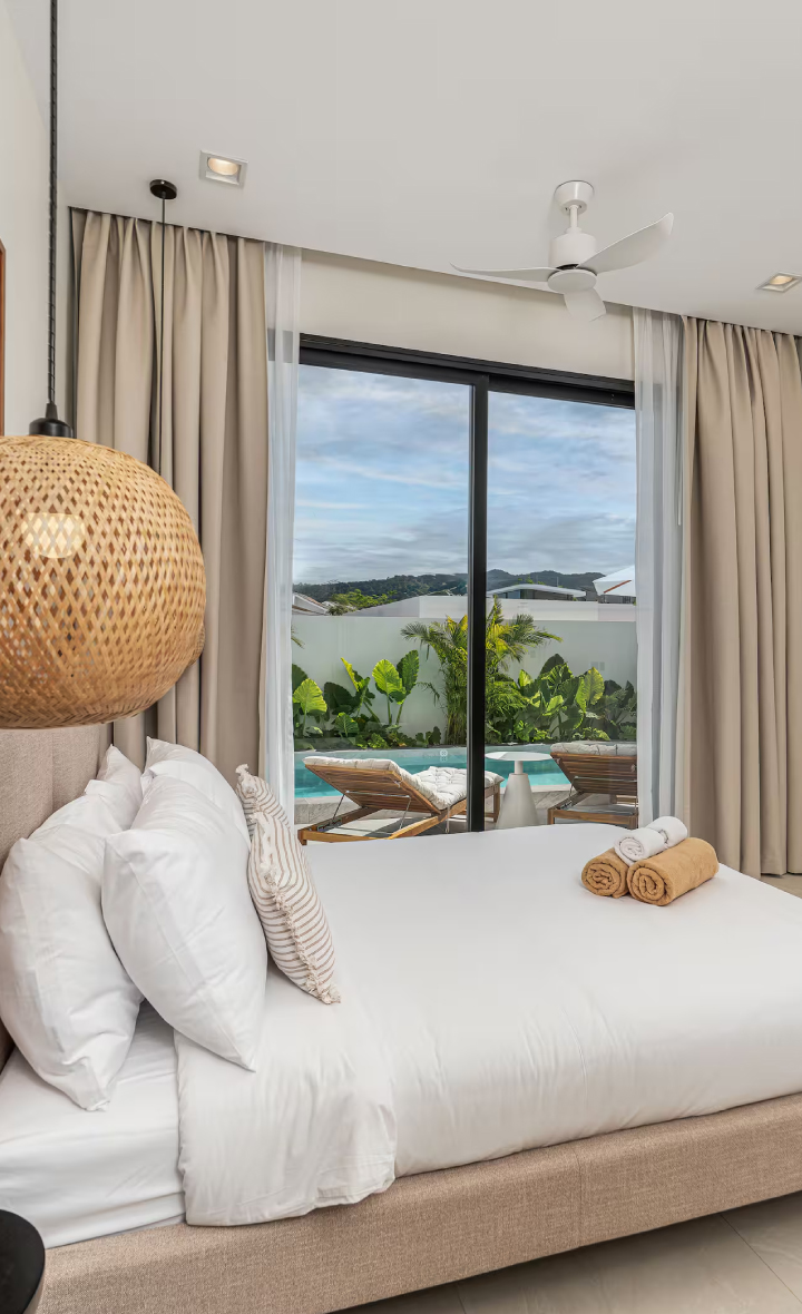Cozy bedroom view of tropical pool villas Bangtao Phuket, with pool and greenery outside.